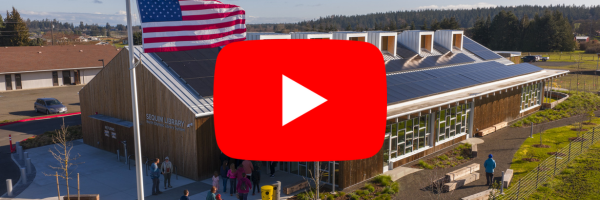 Aerial photo of the front of the new Sequim Library with a play symbol in front of it.